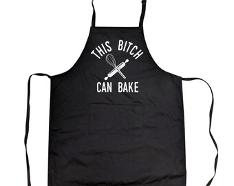 May include: A black apron featuring a white graphic of a whisk and a rolling pin crossed in the center. Above and below the graphic, the text reads "THIS BITCH CAN BAKE" in white capital letters. The apron includes a single front pocket and ties.