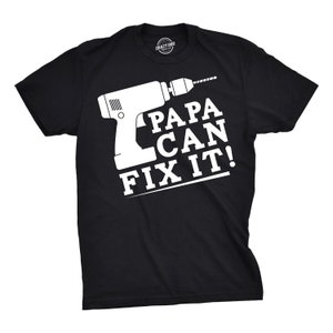 May include: Black t-shirt with a white graphic of a drill and the text "PAPA CAN FIX IT!". The shirt has a crew neck and short sleeves. The brand logo "CRAZY DOG" is printed on the neck.
