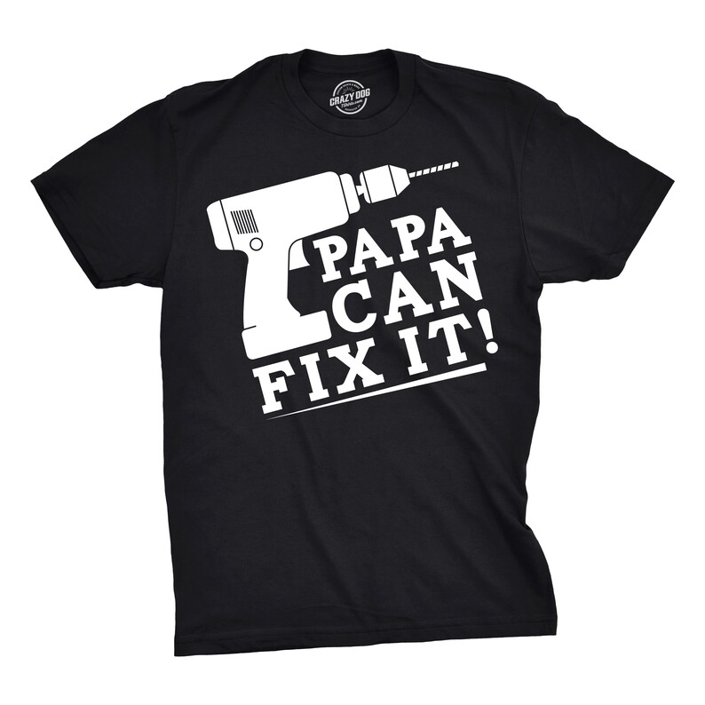 May include: Black t-shirt with a white graphic of a drill and the text "PAPA CAN FIX IT!". The shirt has a crew neck and short sleeves. The brand logo "CRAZY DOG" is printed on the neck.