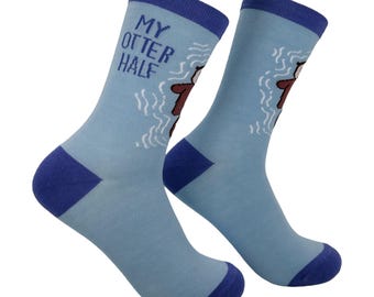 May include: A pair of light blue crew socks with dark blue cuffs, heels, and toes. The socks feature a brown otter graphic surrounded by white water ripples and the text "MY OTTER HALF" printed in dark blue lettering on the side.