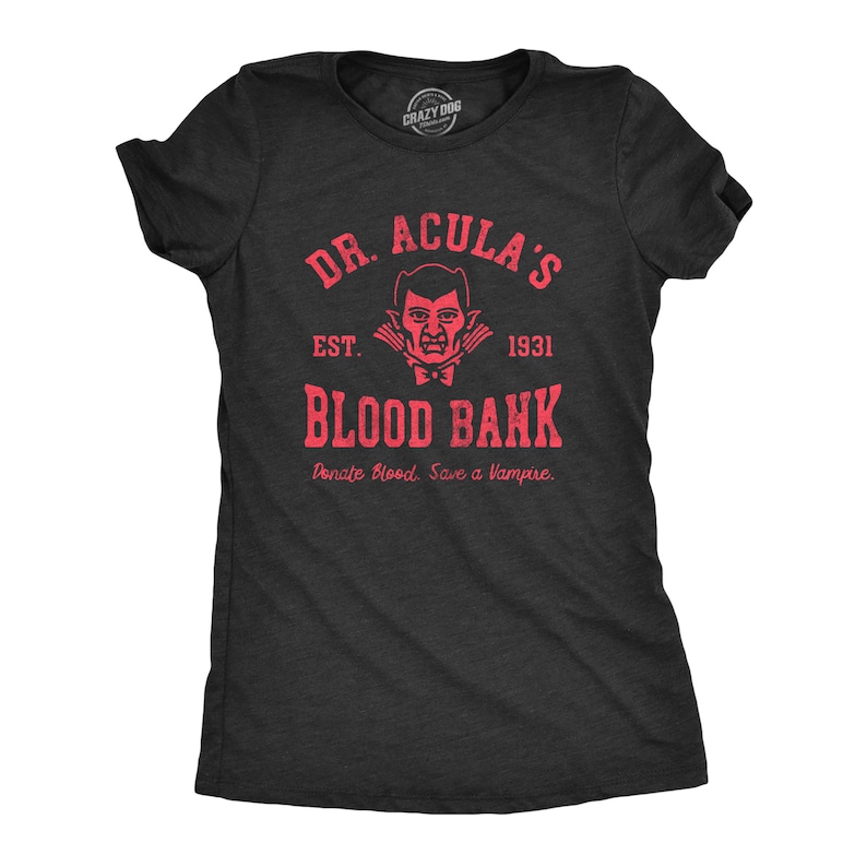 Puede incluir: Una camiseta negra con un estampado rojo de un vampiro con el texto "Dr. Acula's Blood Bank Est. 1931 Donate Blood. Save a Vampire."