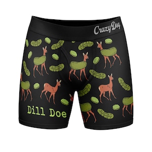 May include: Black boxer briefs featuring a repeating pattern of brown deer with green pickles on their backs and scattered pickle slices. The waistband displays the text Crazy Dog, and the lower left leg features the text Dill Doe in green.