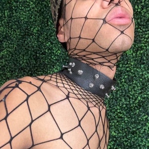 May include: A person wearing a black fishnet top with a black leather choker with silver studs.
