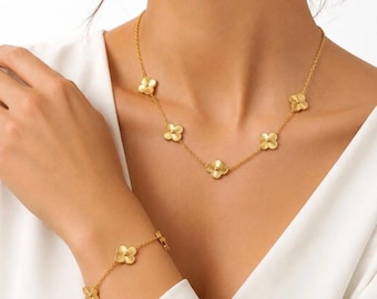 Puede incluir: Un conjunto de collar y pulsera en tono dorado que presenta una cadena delicada con dijes en forma de trébol de cuatro hojas espaciados uniformemente. Cada trébol tiene un acabado dorado mate texturizado y un pequeño detalle central.