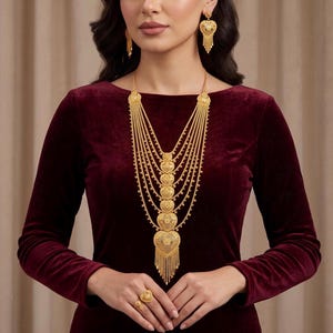 Puede incluir: Un conjunto de joyería en oro que consta de un collar de varias capas con colgantes en forma de corazón y flecos, pendientes colgantes a juego en forma de corazón y un anillo a juego, todo con filigrana y metal texturizado.