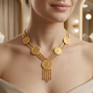 Puede incluir: Un collar dorado con colgantes circulares en forma de monedas. El collar presenta un colgante central con detalles de cadenas colgantes. El diseño incluye múltiples colgantes de monedas conectados por finas cadenas. El collar es usado.
