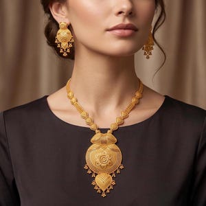 Puede incluir: Un conjunto de joyería de oro que consta de un collar y pendientes a juego. El collar presenta un gran colgante circular con intrincados grabados florales y elementos colgantes, suspendido de una cadena de eslabones texturizados en forma de corazón.