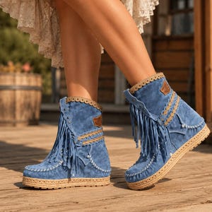 Puede incluir: Botines de ante azul con flecos largos, un borde festoneado en color beige a lo largo del cuello y una suela de plataforma de yute trenzado. Los botines incluyen costuras blancas en la puntera y los laterales, además de un pequeño parche marrón.