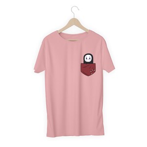Pu&ograve; includere: T-shirt rosa chiaro con tasca rossa scuro. La tasca contiene un personaggio dei cartoni animati in bianco e nero. Il design del personaggio &egrave; semplice.
