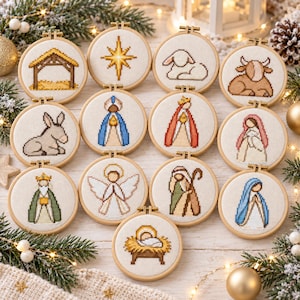 Könnte beinhalten: Eine Sammlung von dreizehn runden Holzstickrahmen mit Kreuzstichmotiven von Krippenfiguren, darunter ein Stall, ein Stern, Tiere, Engel und heilige Figuren, präsentiert auf einer weißen Oberfläche mit weihnachtlichem Tannengrün.