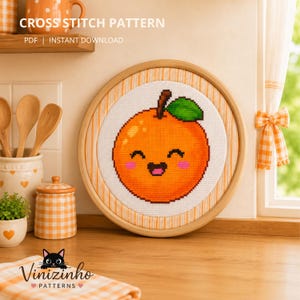 May include: A cross stitch pattern featuring a bright orange fruit with a smiling face, pink cheeks, and a green leaf, displayed in a round wooden embroidery hoop. The text reads CROSS STITCH PATTERN PDF | INSTANT DOWNLOAD.