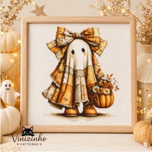 May include: A cross-stitch pattern in a light wood frame featuring a ghost wearing a large plaid bow and a plaid cape, holding a small pumpkin filled with flowers. The ghost has two black eyes and is rendered in shades of orange, brown, and white.