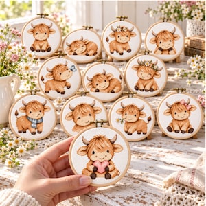 May include: A collection of circular wooden embroidery hoops featuring cross-stitch designs of fluffy brown highland calves. Each hoop displays a unique calf, some with accessories like a blue scarf, a pink bow, or a heart, set against white fabric.