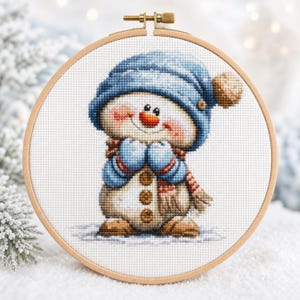 Peut inclure: Une broderie au point de croix représentant un bonhomme de neige portant un bonnet bleu à pompon, des moufles bleues et une écharpe rayée rouge et blanche. Il a un nez en carotte, des joues roses et trois boutons marron, encadré dans un tambour.