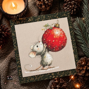 May include: A square cross-stitch embroidery piece on beige fabric featuring a small grey mouse holding a large, shiny red Christmas ornament. The embroidery is framed by a dark green border with a gold-coloured botanical pattern.