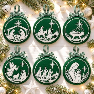 May include: Six circular Christmas ornaments featuring white cross-stitch nativity scenes on a dark green fabric background. Each ornament is topped with a green and white gingham ribbon loop. The designs depict the holy family, the star, and wise men.