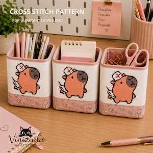 May include: Three cross-stitch pen holders with a capybara design. The holders are white with a pink trim and base, and feature a capybara wearing a nurse's hat and holding a syringe. The text "CROSS STITCH PATTERN" and "PDF | INSTANT DOWNLOAD" is visible.