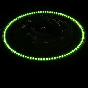 May include: A circular LED light ring glows bright green against a black background. The ring is composed of numerous small, evenly spaced LED lights, creating a continuous illuminated effect. The overall design is modern and sleek.