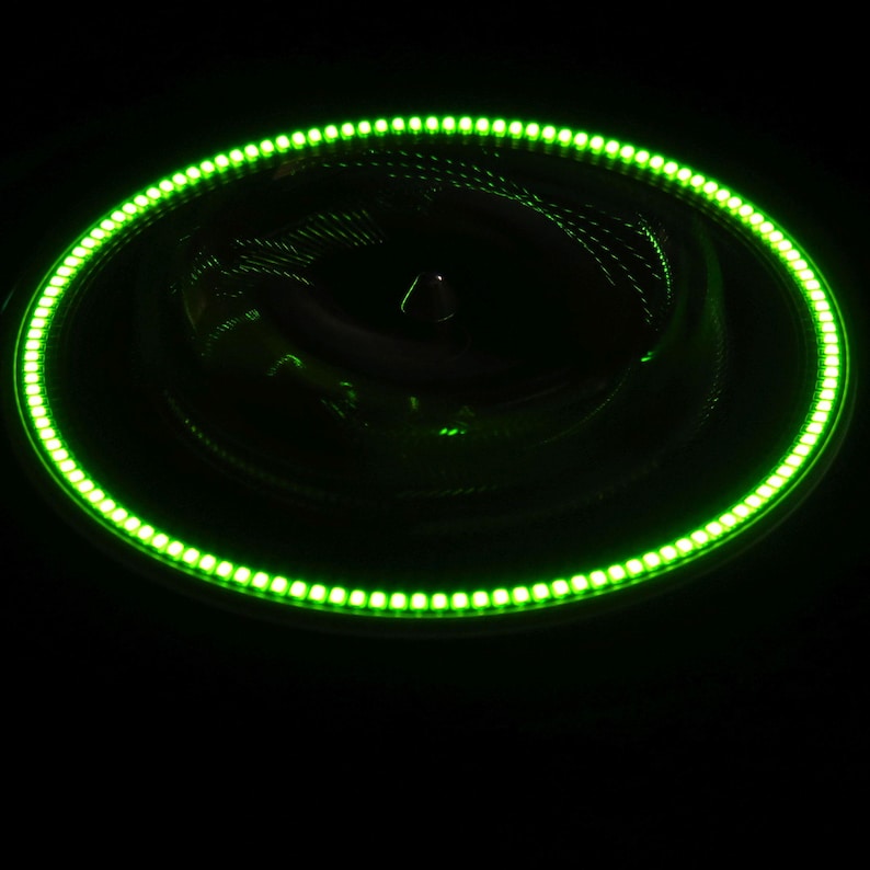 May include: A circular object with a bright green LED light ring. The object appears to be a car accessory, with a dark interior and a central cone-shaped element. The LED ring is composed of numerous small, evenly spaced lights.