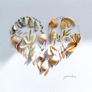Può includere: Un collage a forma di cuore su carta bianca con varie piccole conchiglie disposte a formare fiori e fogliame, accentuato da steli, foglie e punti disegnati a mano con inchiostro marrone. La parola "grünstein" è scritta in corsivo in basso a destra.