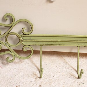 May include: A decorative wall-mounted key-shaped metal rack in a distressed sage green finish. The rack features three hooks for hanging items and an ornate, scrolled design on the key's head. The rack is approximately 24 inches long.
