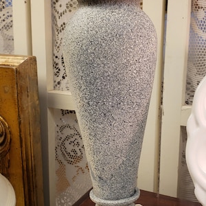 May include: A gray stone candle holder with a decorative top and a base with intricate details. The holder is sitting on a lace tablecloth.