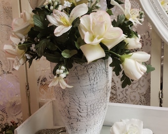 May include: A white ceramic vase with a crackled finish, filled with a bouquet of white and pink roses and alstroemeria flowers. The vase is sitting on a silver tray with a mirrored surface.