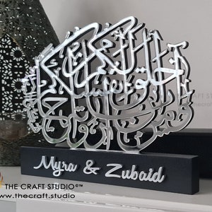Op de afbeelding: Zilveren Arabische kalligrafiekunst met de namen Myra & Zubaid op een zwarte basis. De kalligrafie is op een zilveren achtergrond en de namen zijn in een zilveren lettertype. De basis is gemaakt van hout en heeft een zwarte afwerking. De kunst is gemaakt door The Craft Studio.