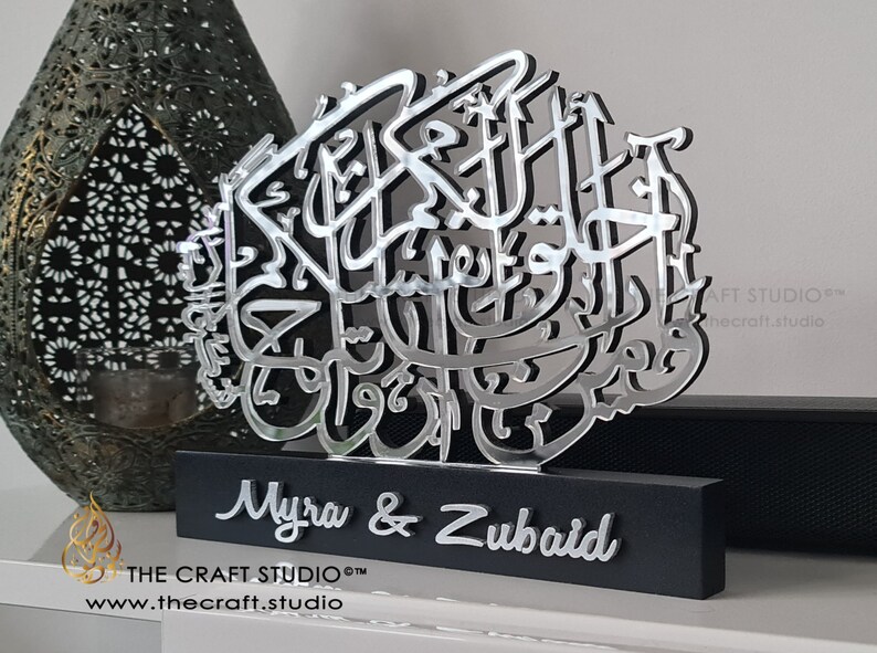 Op de afbeelding: Zilveren Arabische kalligrafiekunst met de namen Myra & Zubaid op een zwarte basis. De kalligrafie is op een zilveren achtergrond en de namen zijn in een zilveren lettertype. De basis is gemaakt van hout en heeft een zwarte afwerking. De kunst is gemaakt door The Craft Studio.