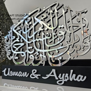 Op de afbeelding: Zilveren spiegelende acrylkalligrafiekunst met de namen Usman & Aysha op een zwarte basis.