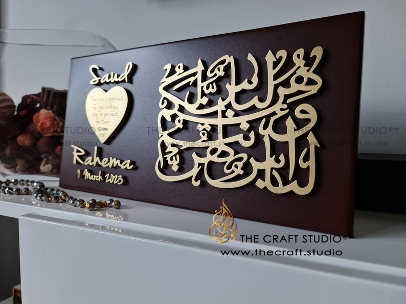May include: A wooden plaque featuring a gold Arabic calligraphy design and the names Saud and Rahema, with the date 1 March 2023. The plaque has a heart-shaped cutout containing a message.