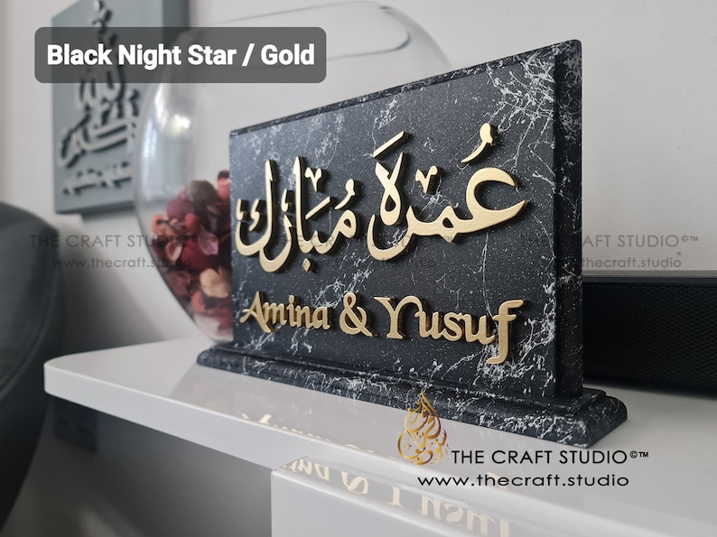 Peut inclure: Plaque noire effet marbre avec lettrage dor&eacute; "عمرة مبارك" et "Amina & Yusuf". L'inscription "Black Night Star / Gold" est visible. Le logo et le site web de The Craft Studio sont pr&eacute;sents.