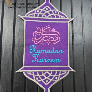 May include: A purple embroidered Ramadan Kareem patch with a lantern design. The patch features Arabic calligraphy in pink and the words "Ramadan Kareem" in teal. The design is outlined in silver thread.