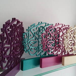 May include: Four wooden wall decor pieces with intricate calligraphy designs. The pieces are painted in shades of purple, teal, pink, and cream.