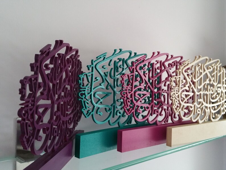 May include: Four wooden wall decor pieces with intricate calligraphy designs. The pieces are painted in shades of purple, teal, pink, and cream.
