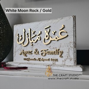 Peut inclure: Plaque d&eacute;corative blanche et dor&eacute;e avec calligraphie arabe et le texte "Ayaz & Family". La plaque a une texture marbr&eacute;e et est inscrite d'une date. Le texte "White Moon Rock / Gold" est en haut.