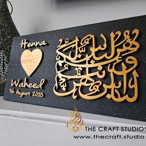 May include: A black rectangular plaque with gold lettering. The plaque features the names "Henna" and "Waheed" with the date "9th August 2023". A gold heart with a message is also included. The plaque has a sparkly black background.