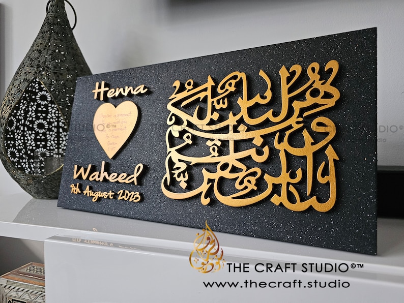 May include: A black rectangular plaque with gold lettering. The plaque features the names "Henna" and "Waheed" with the date "9th August 2023". A gold heart with a message is also included. The plaque has a sparkly black background.