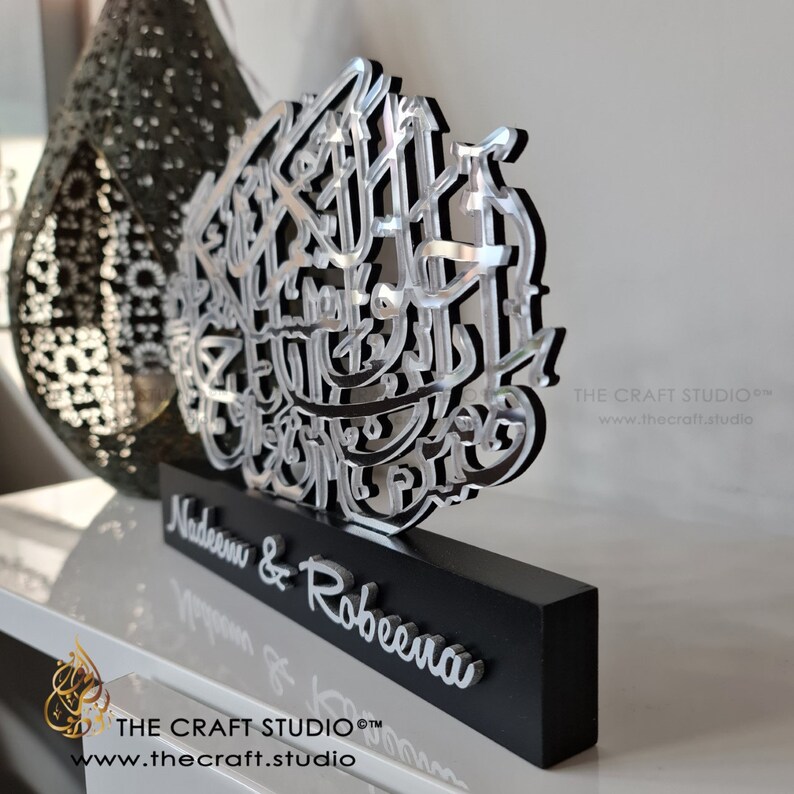 Op de afbeelding: Een zilveren en zwarte decoratieve plaquette met Arabische kalligrafie en de namen Nadeem & Robeena. De plaquette staat op een zwarte basis met de tekst "THE CRAFT STUDIO&trade;" en "www.thecraft.studio" aan de onderkant.