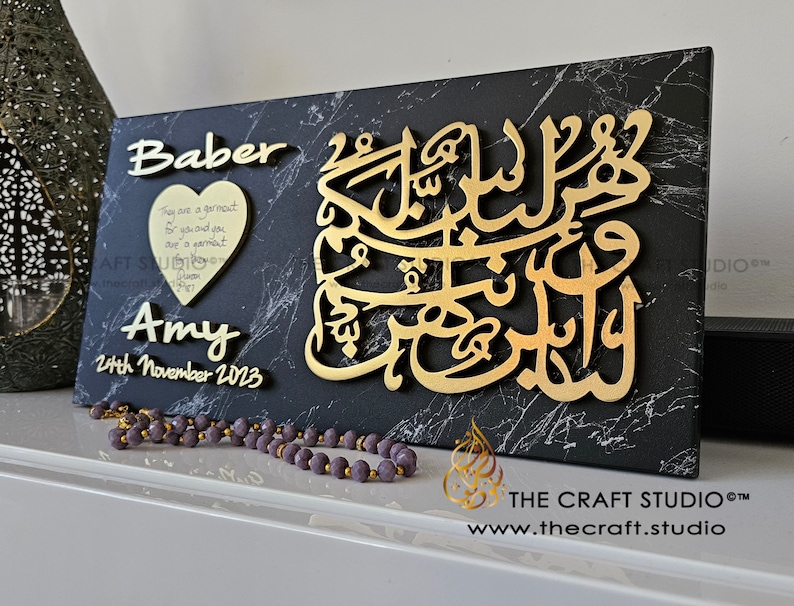 May include: A black and gold wooden plaque with the names "Baber" and "Amy" and the date "24th November 2023". The plaque also features a gold Arabic calligraphy design and a small heart-shaped plaque with a quote about love.