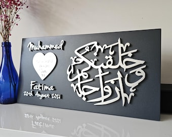 May include: A rectangular dark grey plaque featuring white 3D lettering. The text reads "Muhammed" and "Fatima 20th August 2021" alongside a white heart shape. A large circular white Arabic calligraphy design is positioned on the right side.