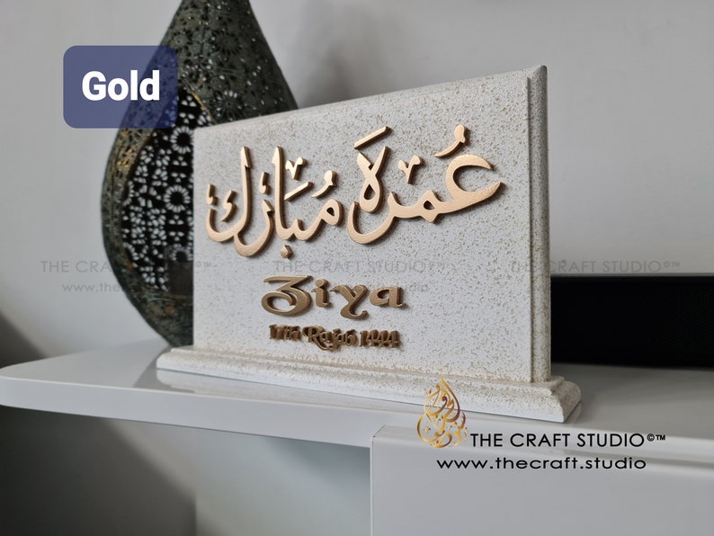 Peut inclure: Panneau d&eacute;coratif dor&eacute; avec calligraphie arabe et le nom "Siya". Le panneau est pos&eacute; sur une base textur&eacute;e blanc cass&eacute; de forme rectangulaire. Le mot "Gold" est dans le coin sup&eacute;rieur gauche.