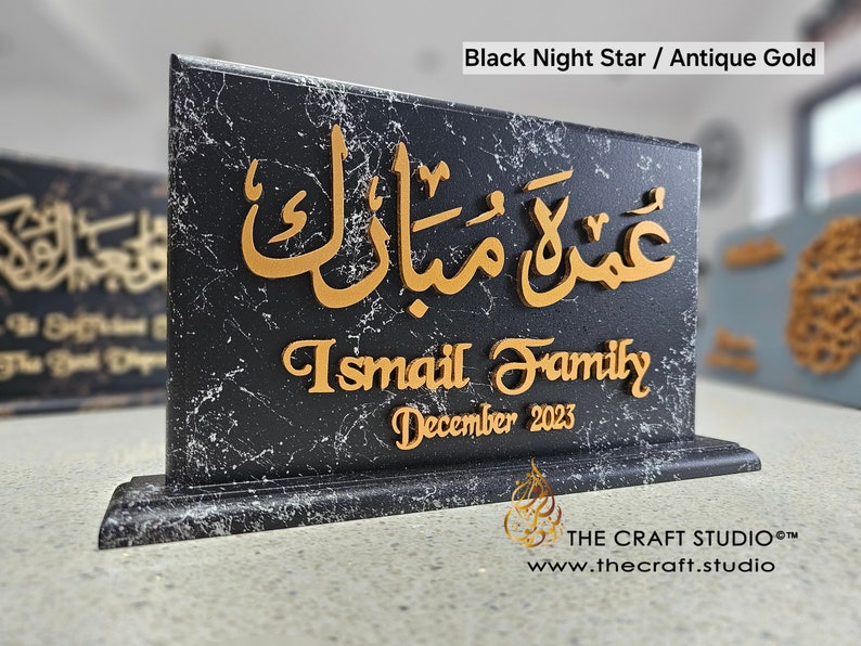 Peut inclure: Plaque noire effet marbre avec calligraphie arabe dor&eacute;e et texte anglais. Le texte indique "Umrah Mubarak", "Ismail Family" et "D&eacute;cembre 2023". La plaque a une base d&eacute;corative et est &eacute;tiquet&eacute;e "Black Night Star / Antique Gold".