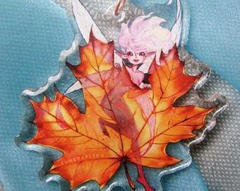 May include: A clear acrylic keychain featuring a fairy inside a fall leaf. The fairy has pink hair and red shoes. The leaf is orange and red with detailed veins. The keychain has a star-shaped clasp and a swivel attachment. The text "YUMEDARLING" is printed on the leaf.