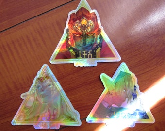 May include: Three holographic stickers featuring characters from the Legend of Zelda: The Wind Waker. The stickers are triangular in shape and feature the words "Power", "Wisdom", and "Courage" in gold lettering. The characters are Ganondorf, Zelda, and Link.