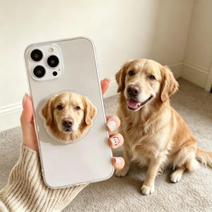 May include: A clear smartphone case featuring a circular adhesive grip on the back, which displays a high-resolution portrait of a golden retriever dog. The case is transparent, revealing the phone's camera lenses and the dog's face.