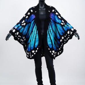 May include: A black crochet butterfly wing shawl with bright blue and turquoise wings, detailed with white spots. The shawl is shown on a mannequin, worn with black clothing and boots. A distinctive, artistic garment.