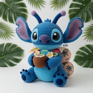 May include: A handmade blue crochet character with large ears, holding a coconut drink with a tiny umbrella. The character has a purple nose and ears, and is wearing a flower lei. The background includes tropical leaves and decorative spheres with the number "626".