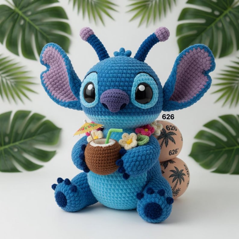 May include: A handmade blue crochet character with large ears, holding a coconut drink with a tiny umbrella. The character has a purple nose and ears, and is wearing a flower lei. The background includes tropical leaves and decorative spheres with the number "626".