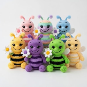 Peut inclure: Sept poupées abeilles crochetées de différentes couleurs, chacune tenant une marguerite blanche. Les abeilles ont des corps rayés et des visages souriants. Couleurs : jaune, rose, violet, vert, bleu et arc-en-ciel.